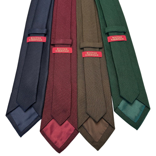Four knitted Grenadine ties in navy, burgundy, brown, and green with 'Rooted & Heritage' labels.