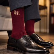 burgundy socks with a logo and black dress shoes on a wooden floor.