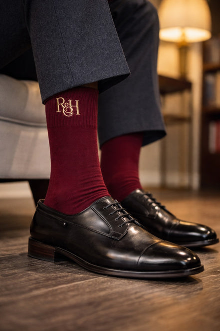 burgundy socks with a logo and black dress shoes on a wooden floor.