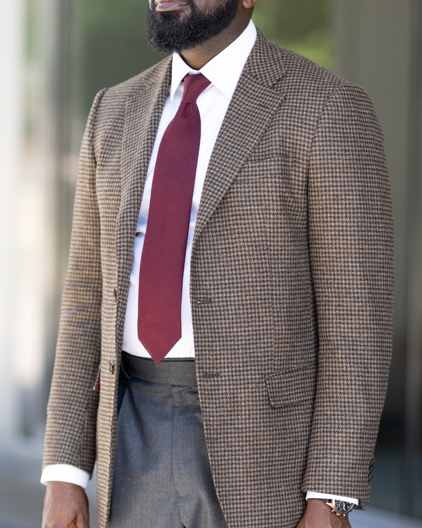 Man wearing a brown houndstooth sport coat, white shirt, and burgundy tie with a blurred background