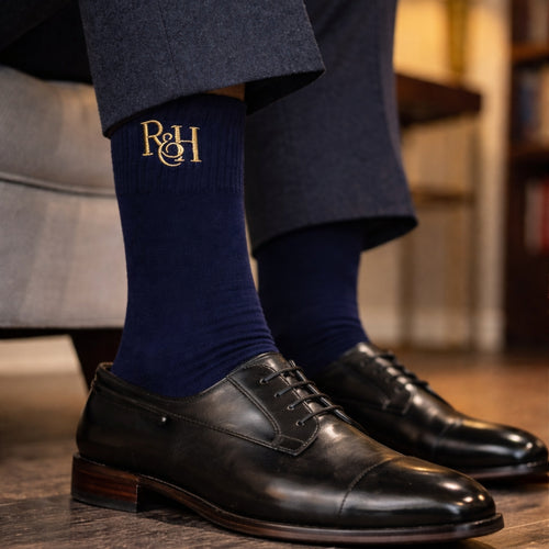 Navy socks with a logo and black dress shoes on a blurred indoor background
