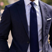 Man wearing a navy suit with a white shirt and navy tie.
