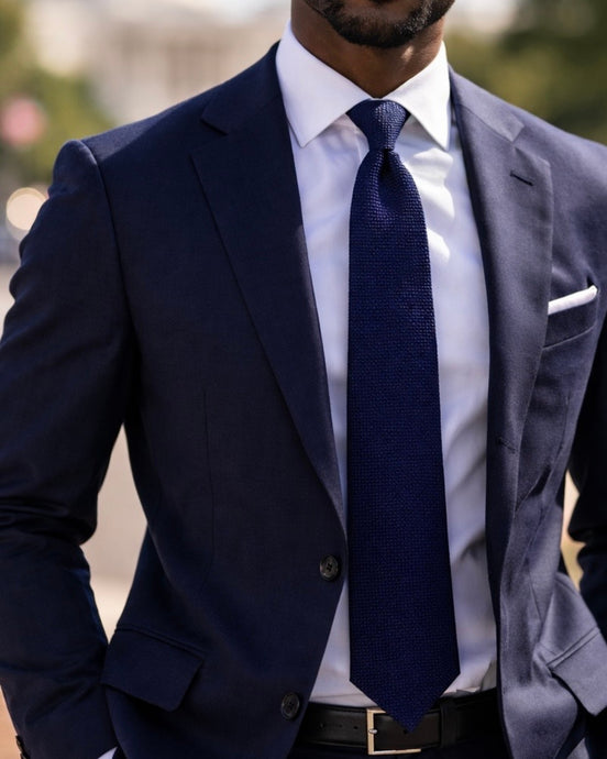 Man wearing a navy suit with a white shirt and navy tie.
