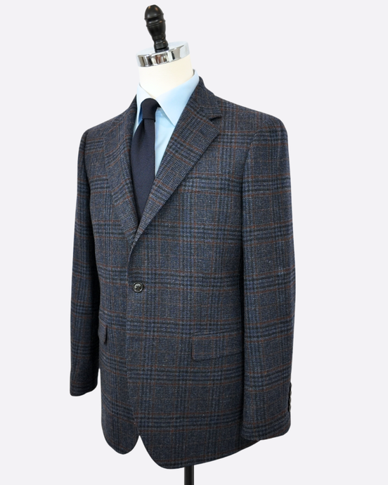 A men's single-breasted plaid suit jacket displayed on a mannequin torso, styled with a light blue dress shirt and a dark tie, against a plain white background.