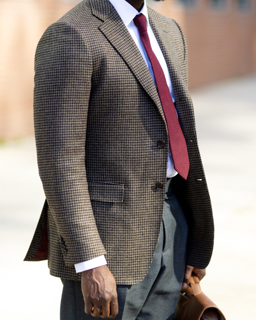 Man wearing a brown checkered suit with a red tie outdoors